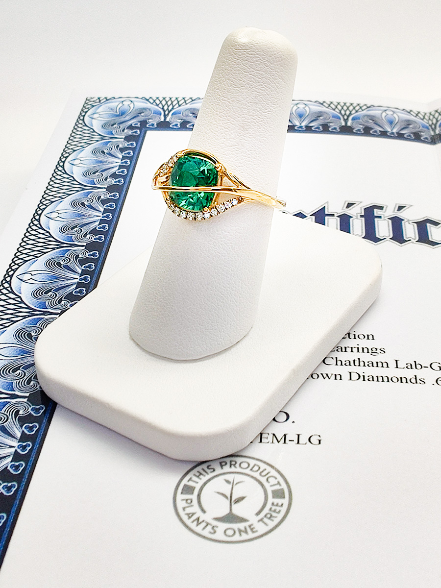 Lab-grown emerald ring on top of Certificate of Authenticity with a stamp that says "THIS PRODUCT PLANTS ONE TREE"
