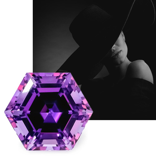 Hexagon Chatham lab grown purple sapphire in front of dark photo of a woman wearing elegant black off-the-shoulder dress and big floppy black hat that hides her eyes